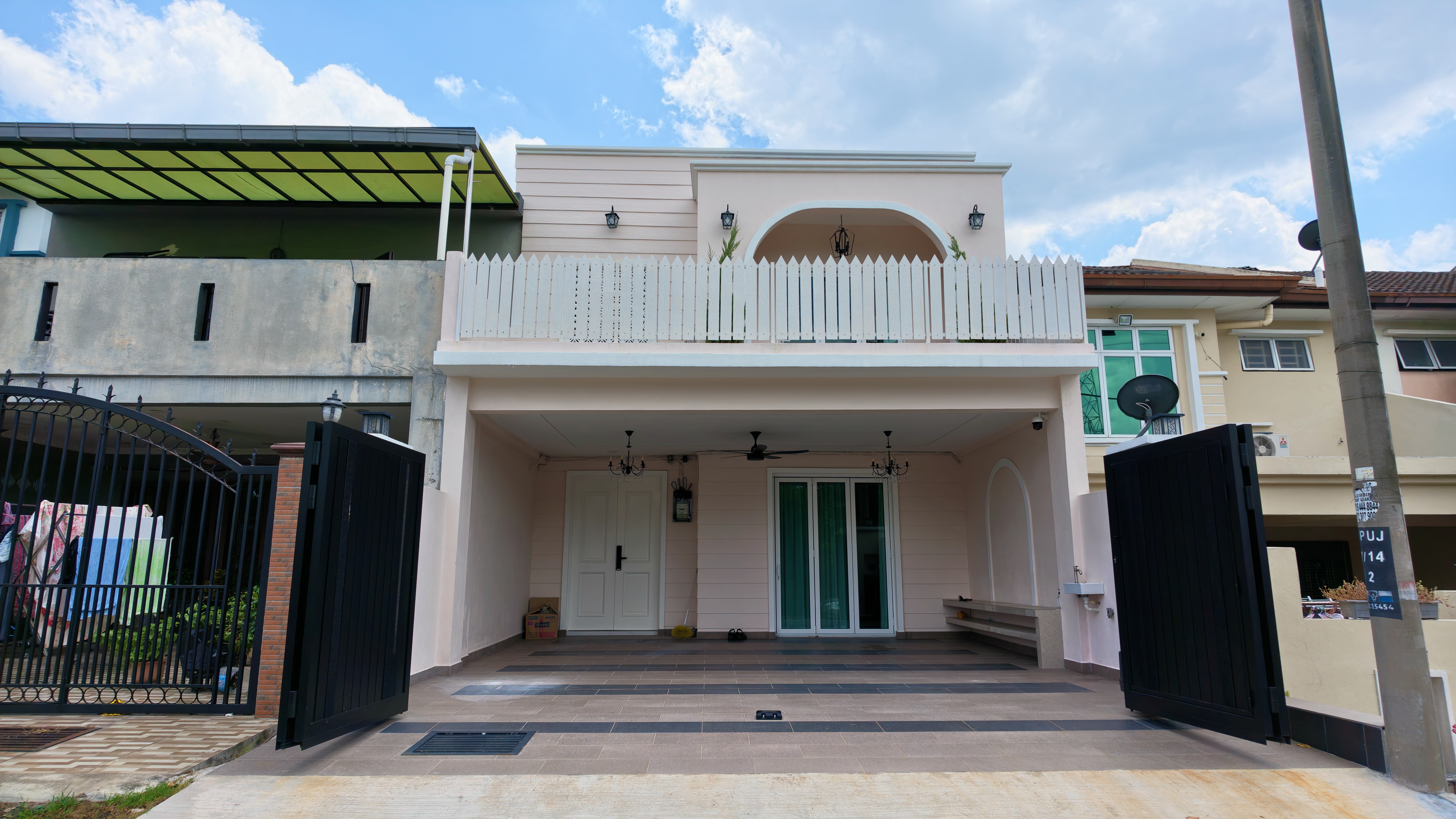 TheRumahPink exterior facade at No. 84, Jalan PUJ 7/14, Puncak Jalil — warm pink 3-storey terrace house with rooftop arch, white picket balcony, and sliding auto gate